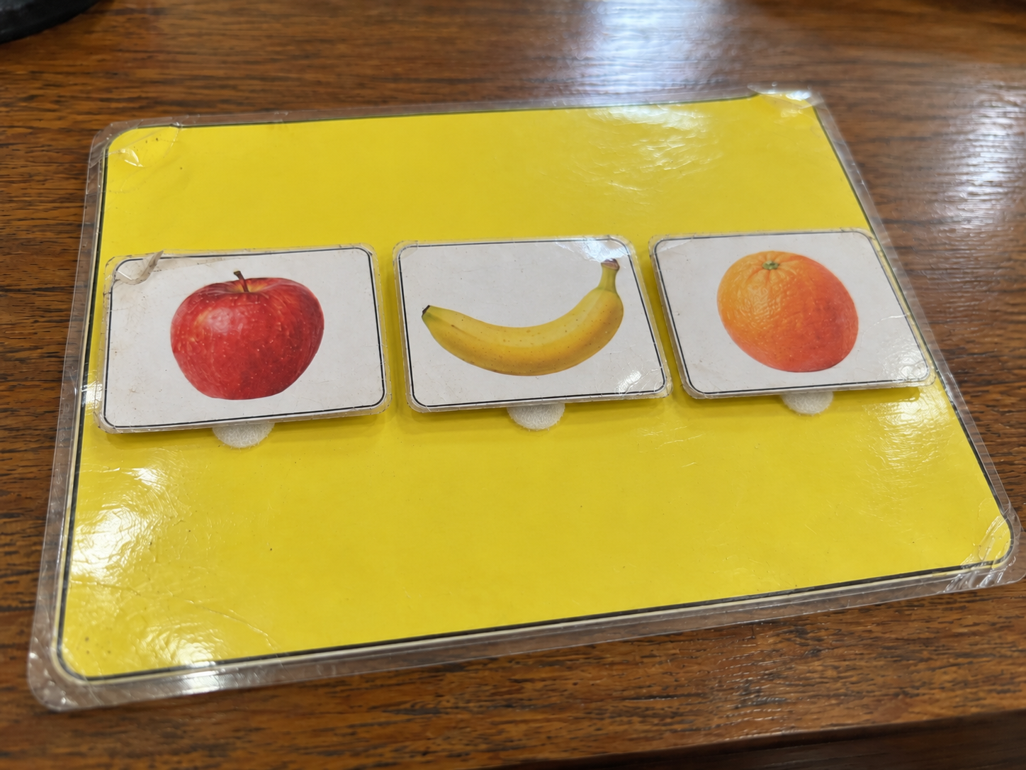 Laminated stimulus learning board with removable apple, banana and orange picture cards.